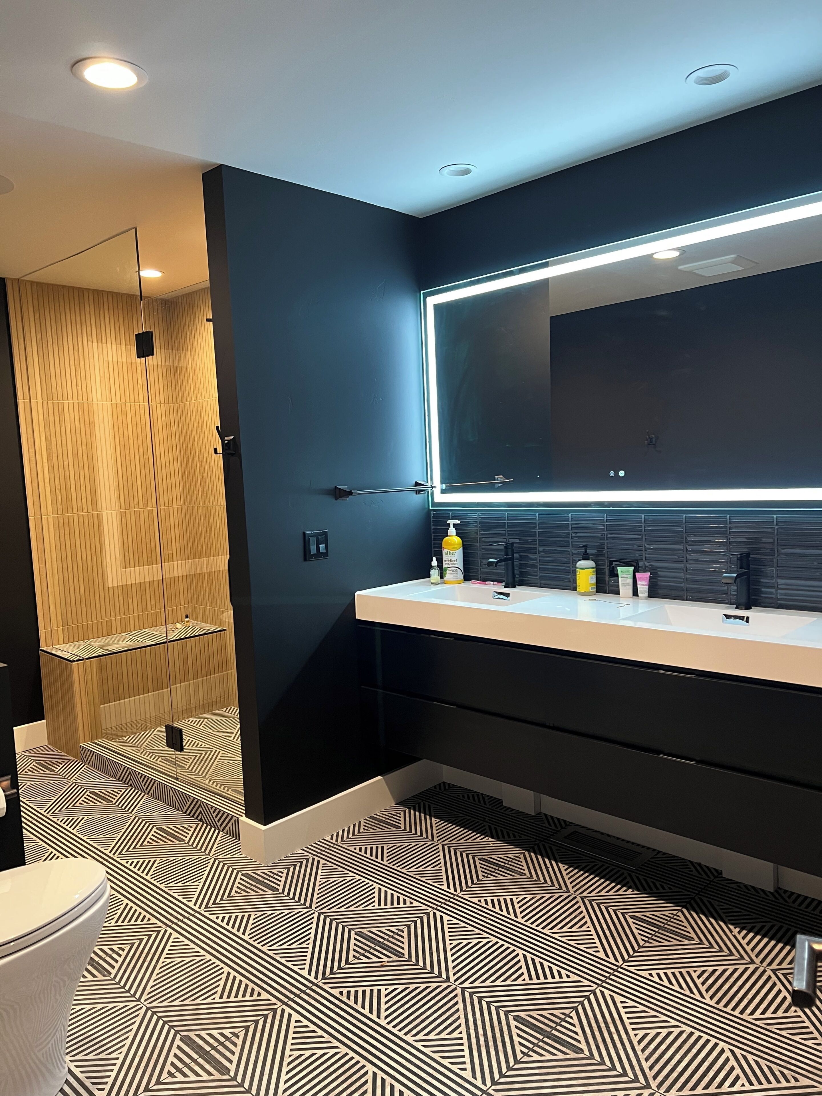 Une salle de bain moderne avec un grand miroir, une cabine de douche et un revêtement de sol à motifs.