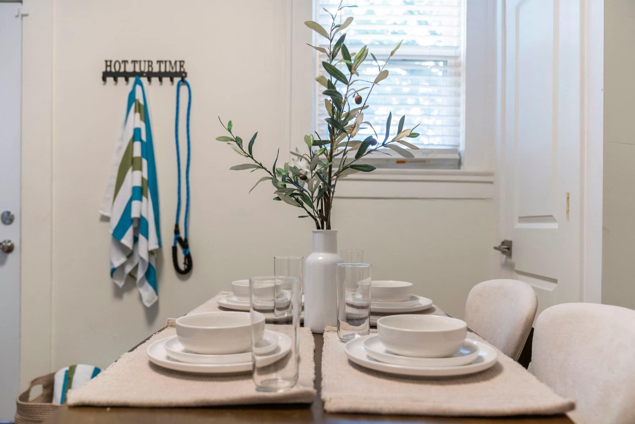 A dining table set with plates, glasses, and a vase with a plant.
