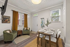 A dining area with a table set for four, a sofa, a small side table, and a door labeled 'HOTEL TIME'. - Hot Tub - Sleeps 9 - Near OSU (Columbus)