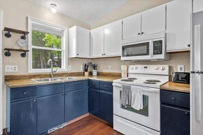 Una cocina con armarios blancos, microondas, estufa y lavamanos.