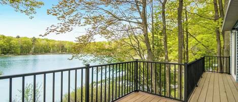 A wooden deck with a black railing overlooking a lake surrounded by trees.