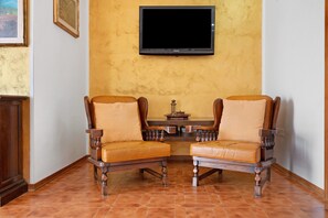 Ein Zimmer mit zwei Holzsesseln mit Ledersitzen, einem an der Wand montierten Flachbildfernseher und einem kleinen Tisch mit Dekoration.