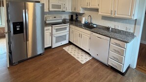 A kitchen with white cabinets, a stainless steel refrigerator, a microwave, an oven, and a granite countertop. - 6 bedroom Farmhouse (Middletown)