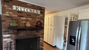 A kitchen with a brick fireplace, white cabinets, and a stainless steel refrigerator. - 6 bedroom Farmhouse (Middletown)