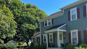 A two-story house with a front porch, a well-maintained lawn, and a large tree. - 6 bedroom Farmhouse (Middletown)