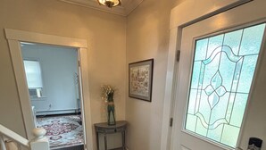 A hallway with a white door, a doormat, a small table with a vase, a framed picture, and a staircase. - 6 bedroom Farmhouse (Middletown)