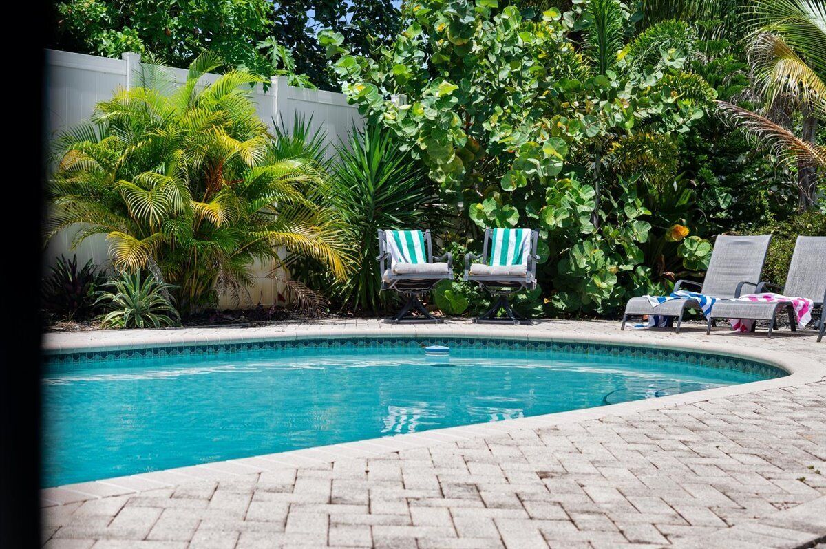 Piscina com espreguiçadeiras, rodeada por vegetação exuberante e um muro branco.