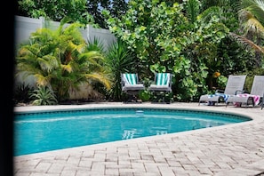 A swimming pool with lounge chairs, surrounded by lush greenery and a white fence. - Atlantic Escape- Delray Pool Retreat (Delray Beach)