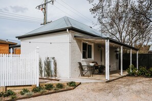 A small white building with a covered patio, a fenced yard, and a tree. - Claret Cottage Walk into Mudgees Historic Heart (Mudgee)