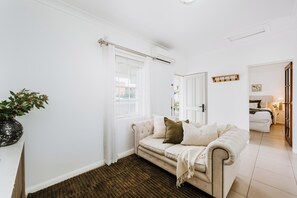 A room with a beige sofa, a white door, and a small table with a plant. - Claret Cottage Walk into Mudgees Historic Heart (Mudgee)