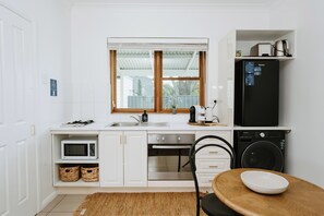 A compact kitchen with white cabinetry, a built-in microwave, a sink, a stove, a dishwasher, and a black refrigerator. - Claret Cottage Walk into Mudgees Historic Heart (Mudgee)