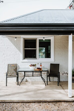 A covered patio with a table and chairs, a window, and a white brick wall. - Claret Cottage Walk into Mudgees Historic Heart (Mudgee)