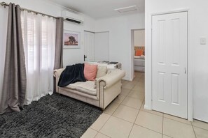 Ein Wohnzimmer mit einem beigen Sofa, einem dunkelgrauen Teppich und einer weißen Tür.