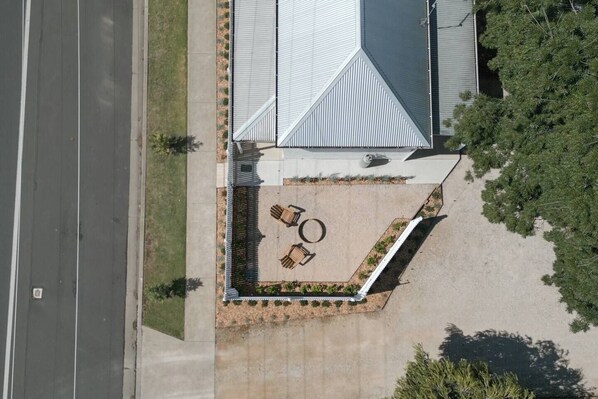An aerial view of a building with a sloped roof, a paved patio with seating, and a road adjacent to the property. - Claret Cottage Walk into Mudgees Historic Heart (Mudgee)