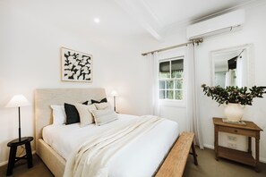 A bedroom with a bed, bedside tables, a lamp, a mirror, a window with curtains, and a framed picture on the wall.