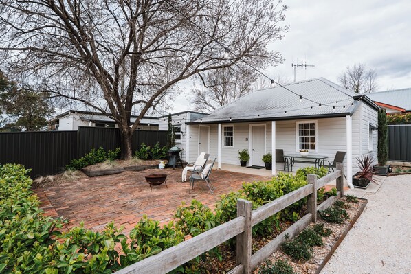 A white house with a brick patio, a wooden fence, and a barbecue grill.