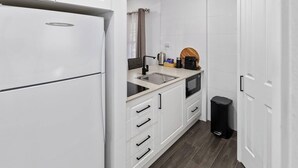 A compact kitchen with white cabinets, a built-in microwave, a sink, and a trash bin.