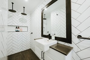 A modern bathroom with a white sink, dark countertop, and a mirror with a dark frame.