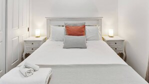 A neatly made bed with a white headboard, two bedside tables with lamps, and a white wall.