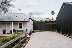 A residential property with a gravel driveway, a wooden fence, and a house with a white exterior and a grey roof.