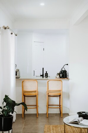 A modern kitchen with two wicker chairs, a countertop with a toaster, a sink, and a mirror. - Ash Cottage Intimate Wine Country Living for Two (Mudgee)
