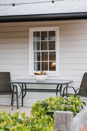 A white exterior wall with a window, a table with chairs, and a potted plant.