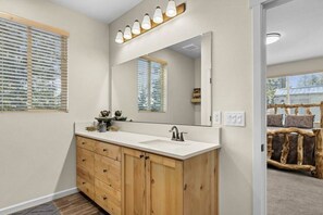 A bathroom with a wooden vanity, a large mirror, and a window with blinds. - Amazing mountain views retreat! (Cle Elum)