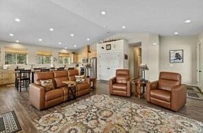 A spacious living area with a brown leather sofa, two leather armchairs, a patterned rug, and a kitchen in the background. - Amazing mountain views retreat! (Cle Elum)