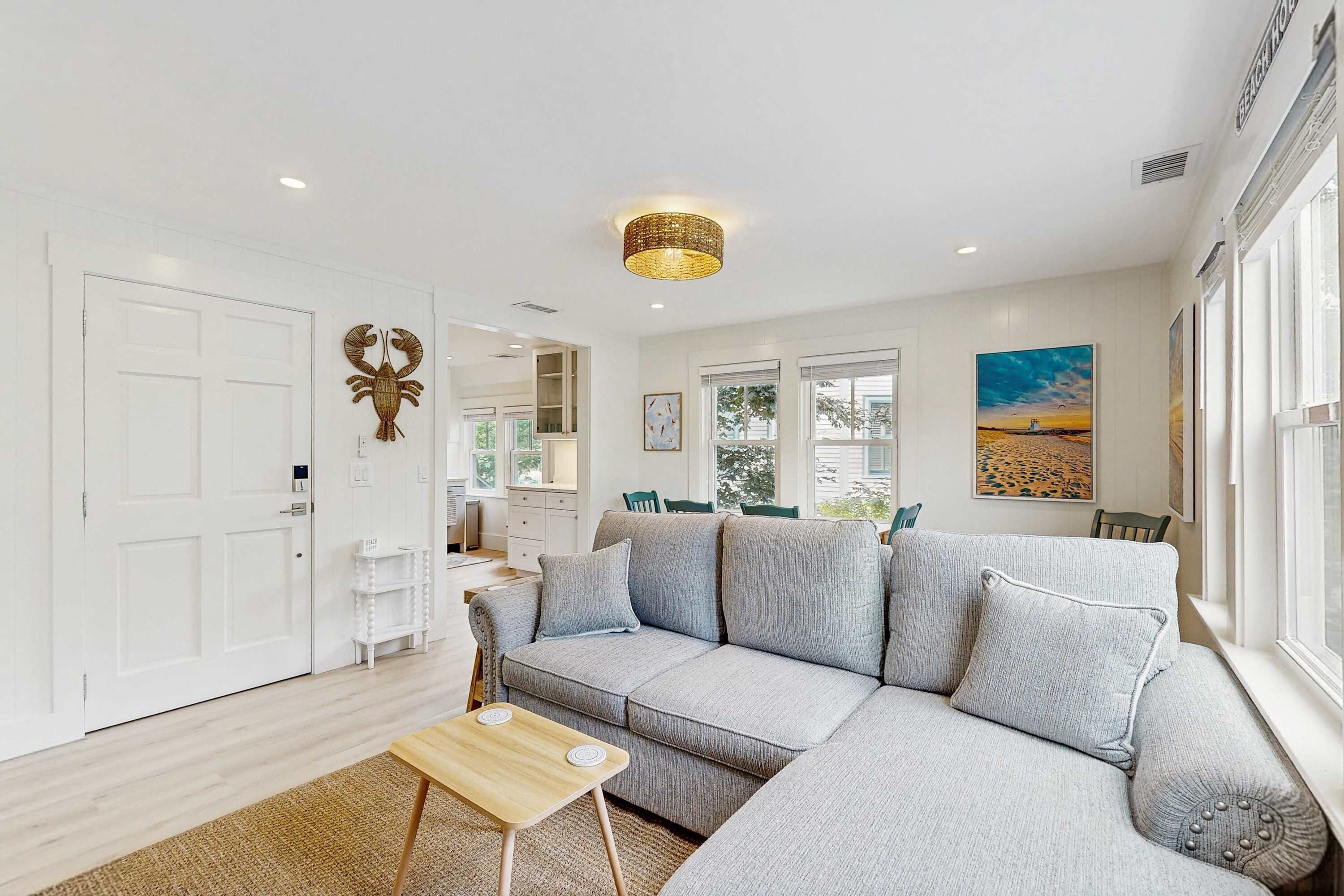 A living room with a grey sofa, a small wooden table, and a large window with a view.