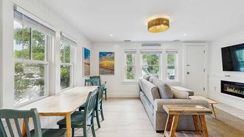 A modern living room with a sofa, a dining table with chairs, a fireplace, and large windows.