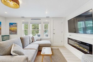 Una sala de estar moderna con un sofá modular, un televisor de pantalla plana, una chimenea y ventanas amplias.