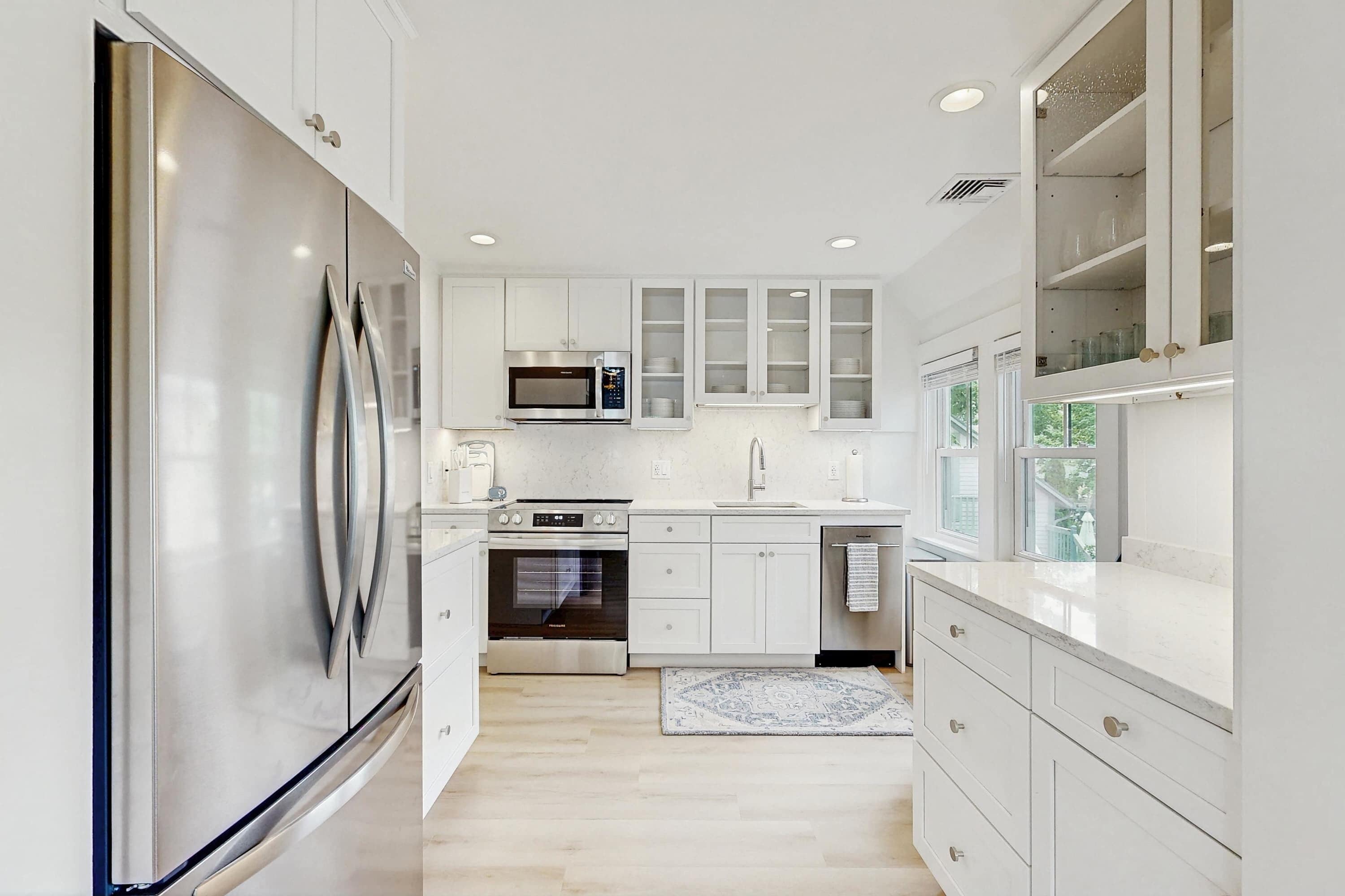 A modern kitchen with stainless steel appliances, white cabinetry, and a large window providing natural light.