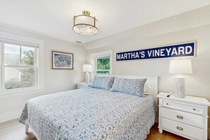 Un dormitorio con una cama, una mesita de noche, una lámpara, un ventanal y un cartel en la pared que dice 'Martha's Vineyard'.