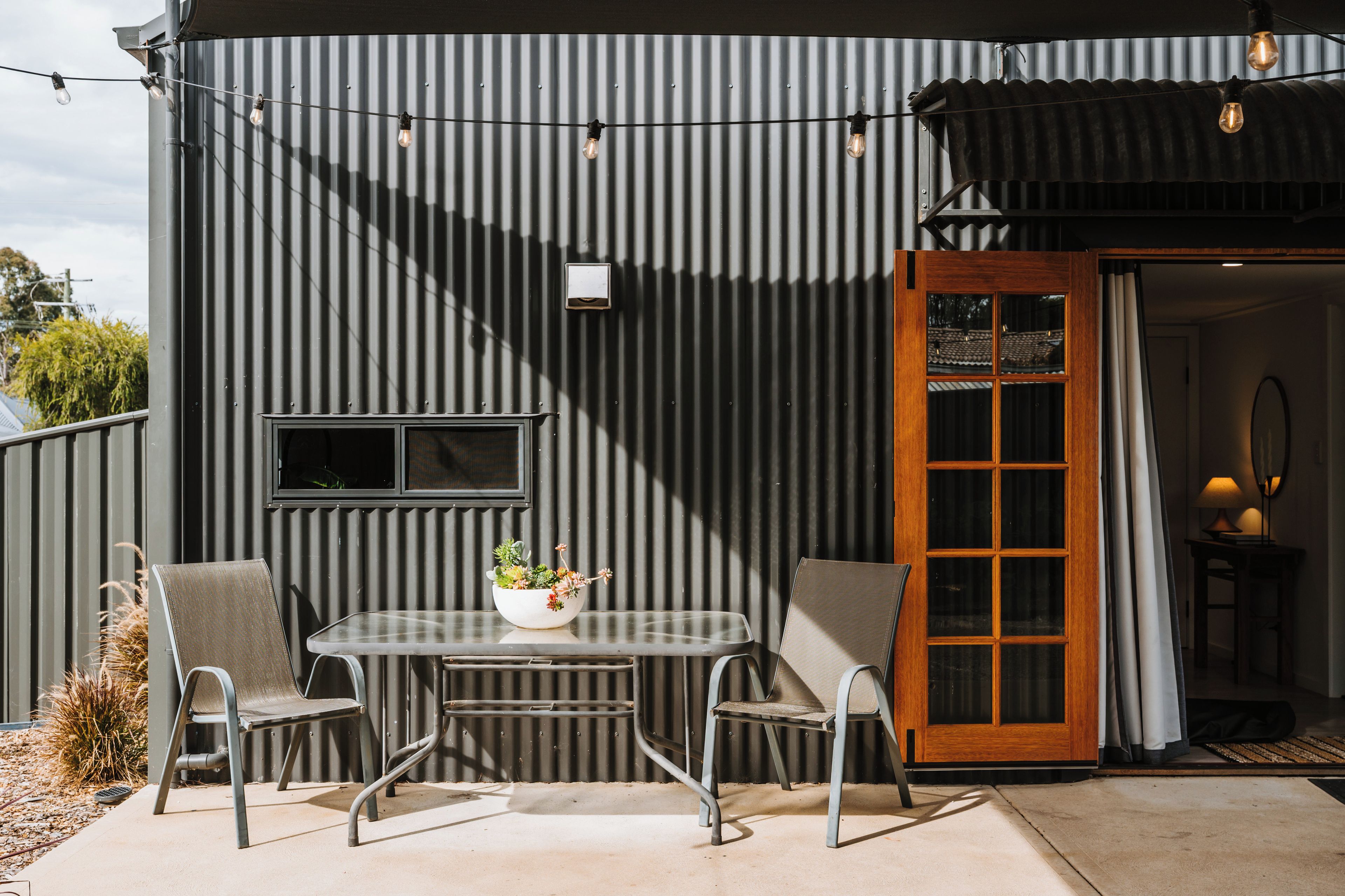 A patio with a table and chairs, a potted plant, and a door leading to an interior space.