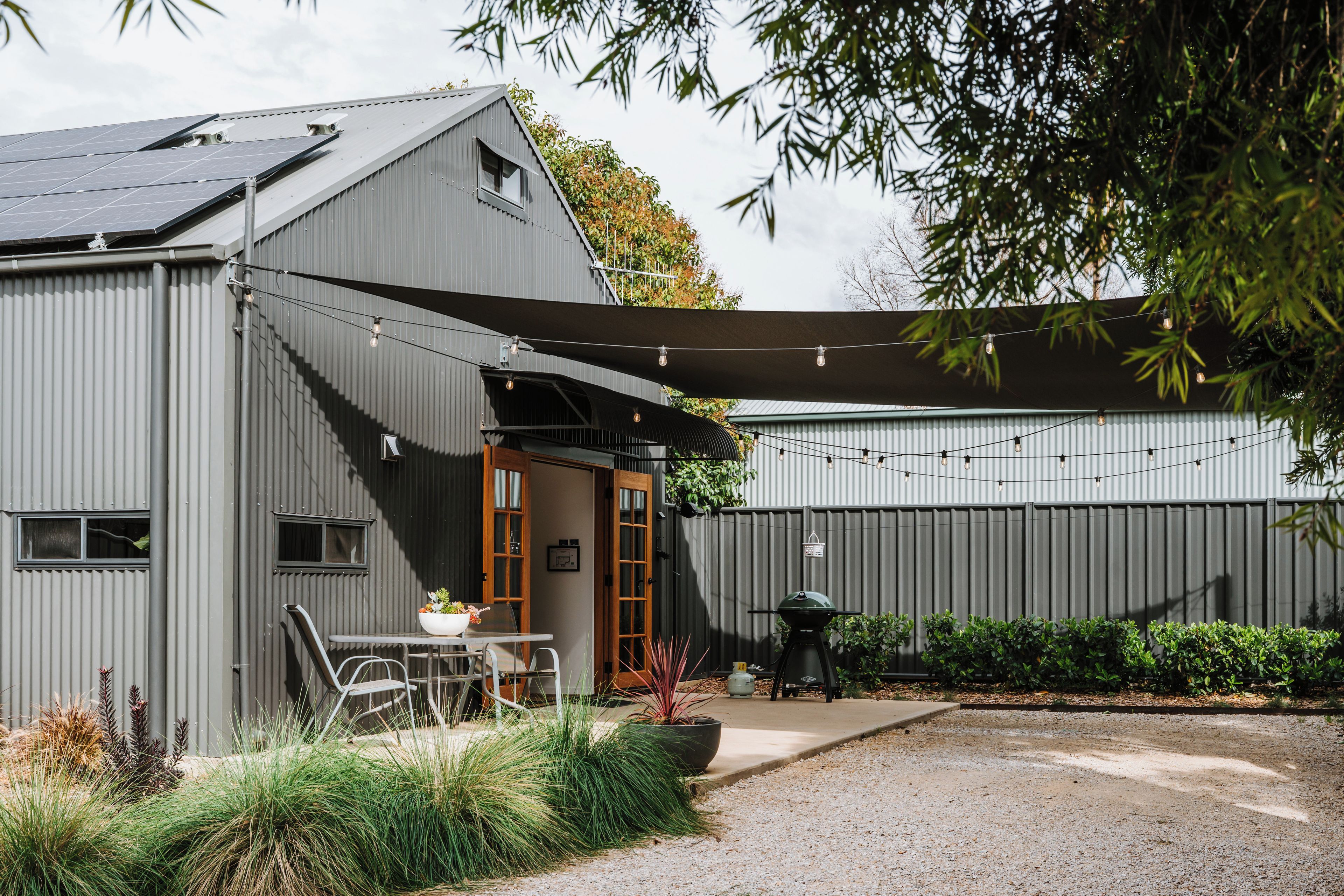 A modern building with a covered patio area, a barbecue setup, and a garden with various plants.