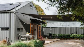 A modern building with a covered patio area, a barbecue setup, and a garden with various plants.