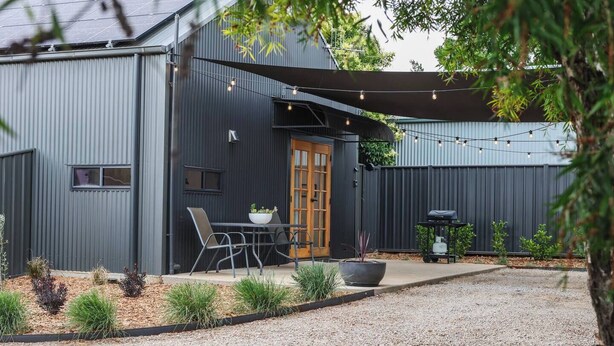 Un patio moderno al aire libre con mesa y sillas, una parrilla y una pérgola con luces colgantes.