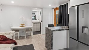 Una cocina moderna con refrigerador empotrado, un comedor con mesa y sillas blancas y un pequeño rincón de descanso con sofá.