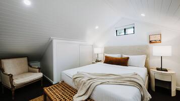 A bedroom with a bed, a chair, a bedside table, a lamp, and a window.