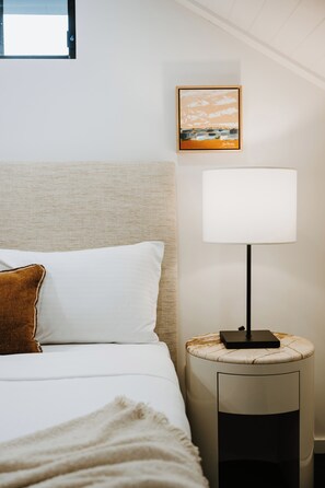A neatly made bed with white linens and a brown pillow, a bedside table with a lamp, and a framed picture on the wall. - Luxe Loft Contemporary Comfort by Mudgees CBD (Mudgee)