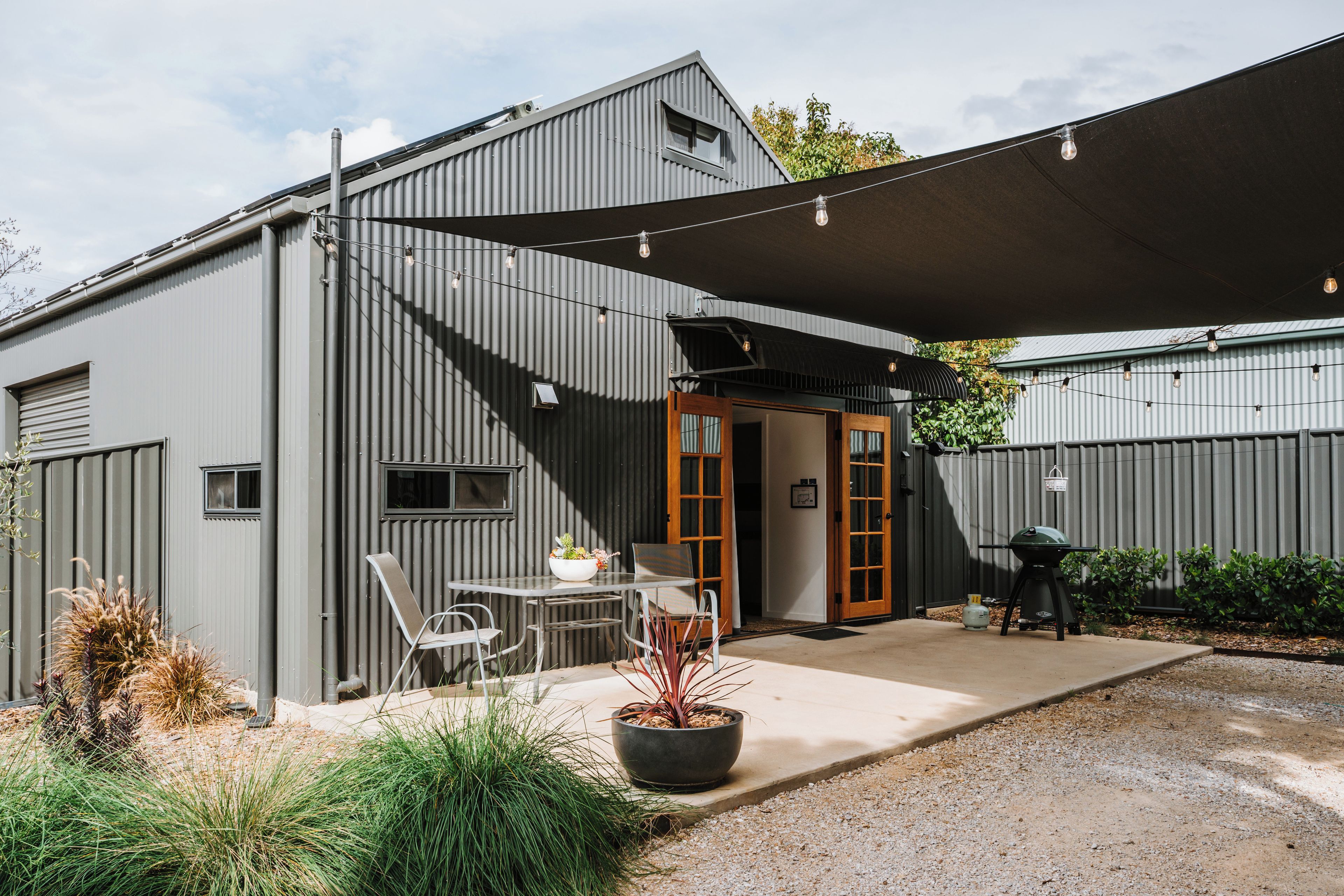 A modern outdoor patio area with a table and chairs, a barbecue grill, and a large shade sail.