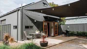 A modern outdoor patio area with a table and chairs, a barbecue grill, and a large shade sail.