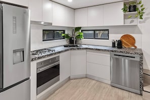 Eine moderne Küche mit Edelstahlgeräten, weißen Schränken, einer Granitarbeitsplatte und einem Holzer Schneidebrett.