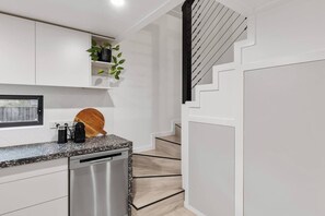 Eine moderne Küche mit weißen Schränken, einer Granitarbeitsplatte, einem Geschirrspüler und einem Holzschneidebrett.