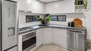 A modern kitchen with stainless steel appliances, white cabinetry, a granite countertop, and a wooden cutting board. - Claret on Douro Three Cottages for Group Getaways (Mudgee)