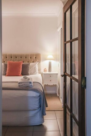 Ein ordentlich eingerichtetes Schlafzimmer mit Bett, Nachttisch, Lampe und einer Tür.