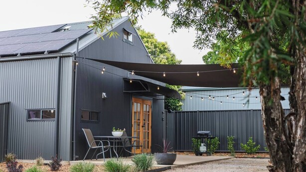 A modern building with a dark exterior, a covered patio with outdoor seating, and a gravel driveway. - Claret on Douro Three Cottages for Group Getaways (Mudgee)