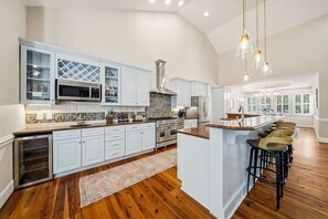 A spacious kitchen with white cabinetry, a central island, and bar stools. - PRIVATE 16+HiddenOasis! SwimPond+HotTub+Sauna+2Firepits+10ac, Pets Welcome! (Hampstead)