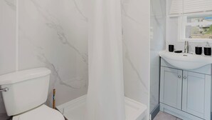 Une salle de bain comprenant des toilettes, un rideau de douche, un lavabo avec un miroir et des placards.