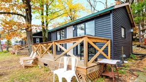 Une cabane dotée d’une terrasse en bois, de deux chaises blanches et d’une petite table.